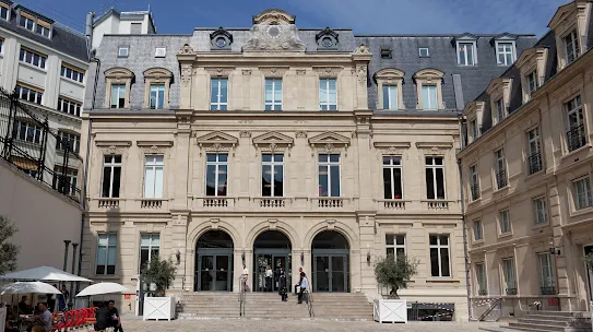 A small group of people talk on the steps of a tan-colored building.